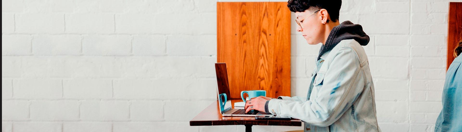 young student using laptop against a white brick wall